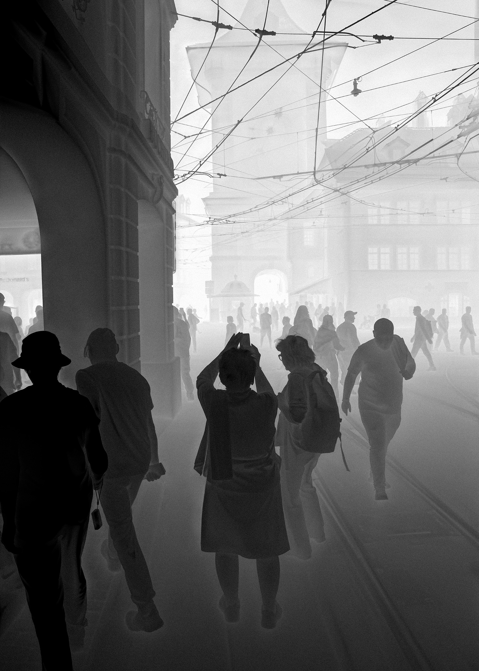 Une vathographie&nbsp;: des passants sous les arcades, sous un réseau de câbles de tram, silhouettes sombres dans une brume pâle.